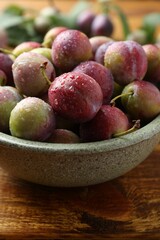 Ripe plums in bowl on wooden table, closeup