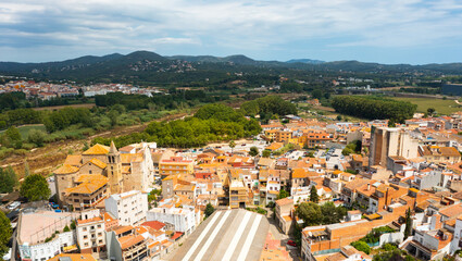 Scenic summer view of tiled roofs of residential houses of Spanish township of Tordera on background of greenery of Montnegre natural park on horizon on sunny day, province of Barcelona, Catalonia