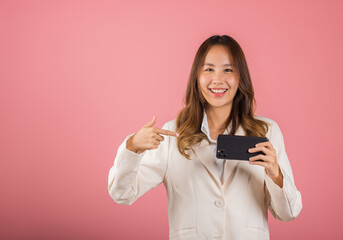 Portrait Asian happy beautiful young woman smile making finger pointing on screen smartphone in hand, female attractive shopping online application isolated studio shot pink background with copy space