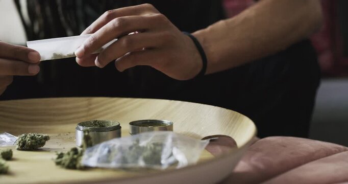 Hands, cannabis and rolling cigarette in home, 420 and prepare weed at table to relax. Closeup of person with marijuana joint, drugs abuse and hemp paper, natural cbd plant or thc addiction in house
