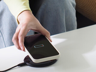 Charging mobile phone battery with wireless charging device in the table. Smartphone charging on a...
