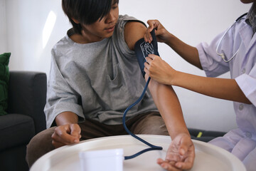 Fototapeta premium Young Asian Guy Medical Checking At Home Using Blood Pressure Test With Doctor