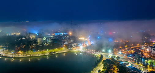 Aerial view of a Da Lat City in the mist magical night, hiden in the fog and clouds. Urban development texture, transport infrastructure. Tourist city in developed Vietnam. Night cityscape