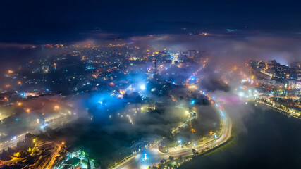 Aerial view of a Da Lat City in the mist magical night, hiden in the fog and clouds. Urban development texture, transport infrastructure. Tourist city in developed Vietnam. Night cityscape