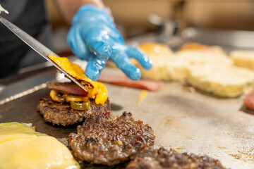 Cook adding cheese on a tasty burger with bacon and mushrooms