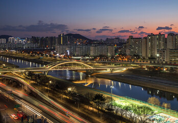 Guro-gu, Seoul, South Korea - February 20, 2022: Night view of car light trajectory on Seobu Expressway against Anyang Bridge on Anyangcheon Stream and apartments