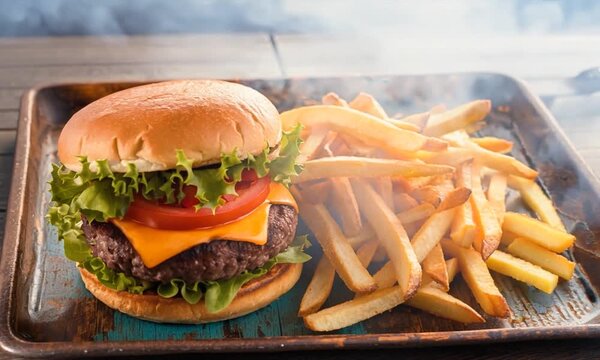 classic burger with lettuce, tomato, and melted cheese, served on a soft bun, accompanied by a generous portion of golden French fries. The meal is presented on a rustic tray, creating a casual and ap