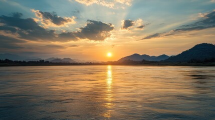 Fototapeta premium The sun is setting over a body of water, casting a warm glow over the landscape