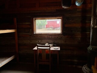 Cuarto oscuro con mesa y silla de madera con vista a una ventana. 