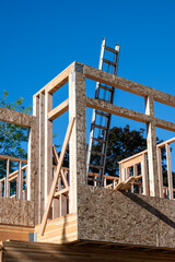Summer construction season, new house build at the framing stage, aluminum extension ladder on 2nd floor leaning against exterior wall, early morning sunny day
