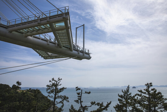 Namhae-gun, Gyeongsangnam-do, South Korea - May 14, 2022: Low angle view of tourists on an observatory with sky swing against sea at Sulli Sky Walk