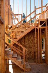 Summer construction season, two story new house build in progress at the framing stage, interior wood staircase on sunny morning
