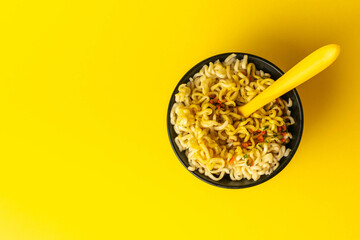 Top View of Instant Noodles in Black Bowl with Yellow Fork on Bright Yellow Background