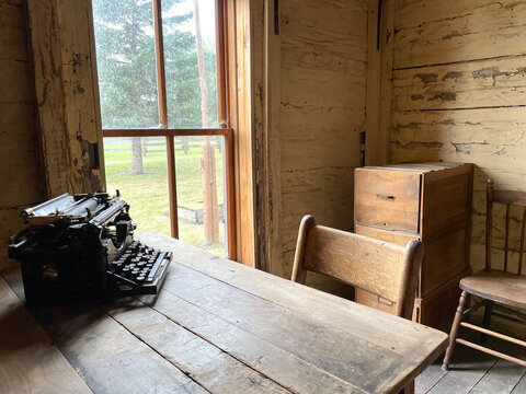 M&aacute;quina de escribir antigua sobre mesa de madera en cuarto con ventana. 