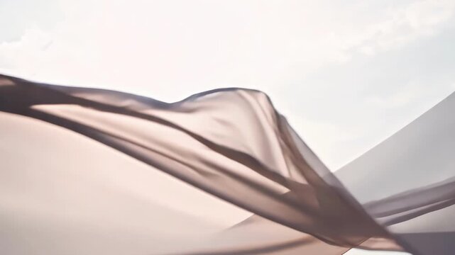 Light pink fabric gently blowing in the wind, creating elegant folds and curves against a serene sky background. The soft and airy nature of the fabric evokes a sense of grace and movement