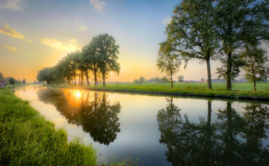 A stunningly picturesque sunset scene beautifully reflecting on a calm and serene river, framed by lush greenery