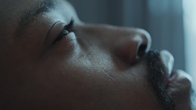 Close-up shot of face of sick Black man wincing slightly in pain as lying in bed at home