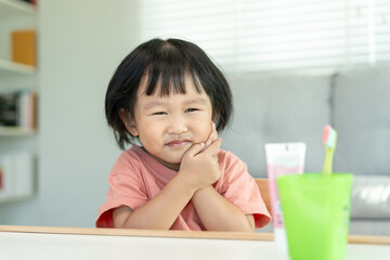 little asian girl presses hand to cheek, suffers from pain in tooth. Teeth decay, dental problems, child emotions and facial expression, oral health care, reducing sweets, fluorine coating