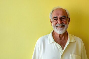 Obraz premium Elderly male presenter, smiling gently, in front of a solid pale yellow background with room for messaging