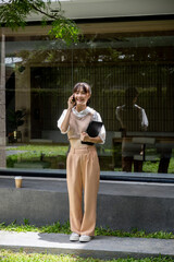 Asian woman in casual clothes is using her smartphone while standing outdoors in a building area