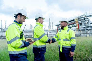 Engineer or technician workers stand on the road near petrochemical factory and shake hands together and discuss about their work.