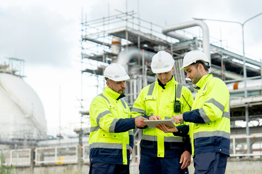 Wide shot engineer or technician workers stand in front of  petrochemical factory and use tablet to discuss their work.
