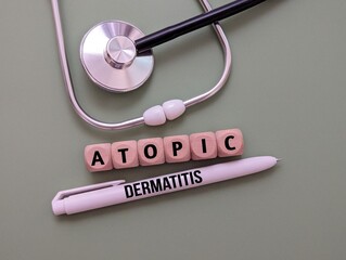 Stethoscope, word atopic dermatitis on wooden cube and pen. the concept of illness
