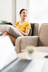 Fototapeta premium Happy young girl using her tablet sits on the sofa at cozy home, looking outside window