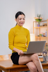 Smiling young asian woman using laptop at home.