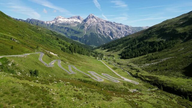 A breathtaking drone view of the Spl&uuml;gen Pass, showcasing a winding road that snakes through majestic mountains. The stunning scenery highlights the dramatic curves and elevation changes of the pass