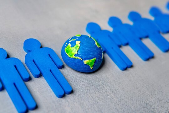 A miniature globe between a row of blue human figures. Interconnectedness of humanity concept.
