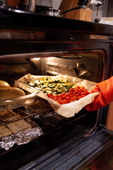 placing a tray of roasted cherry tomatoes and zucchini into the oven