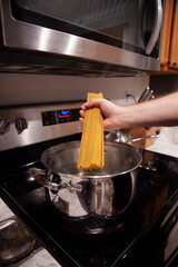 Hand holding uncooked pasta over a pot of boiling water on a stovetop
