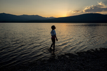Fototapeta premium Silhouette of child standing in a mountain lake at sunset