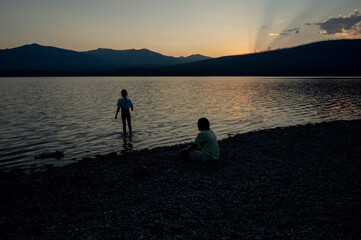 Fototapeta premium Siblings enjoying the sunset at a mountain lake