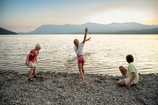 Three children playing on a rocky beach by a mountain lake