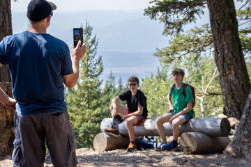 Man photographing two boys sitting on a log in a scenic forest