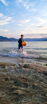 Boy playing with ball in shallow water at beach during sunset