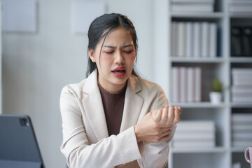 Businesswoman is experiencing wrist pain, likely from prolonged computer use, highlighting the importance of workplace ergonomics