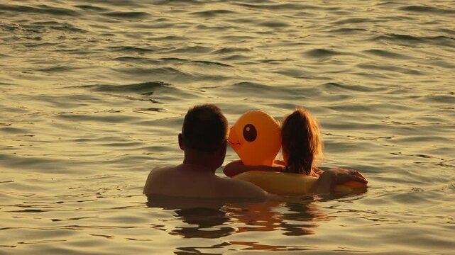 Man with daughter in Floating Duck - Family relaxing on beach in a yellow inflatable ring on the calm waters of the sea on a sunny day.