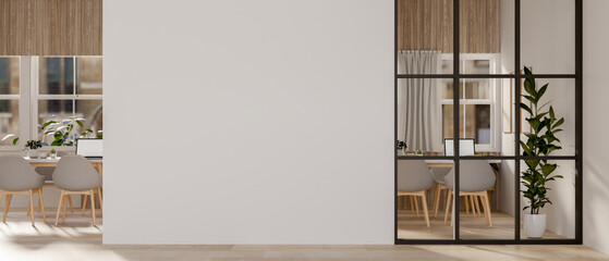 A hallway features an empty white wall and a glass partition that looks into a meeting room.