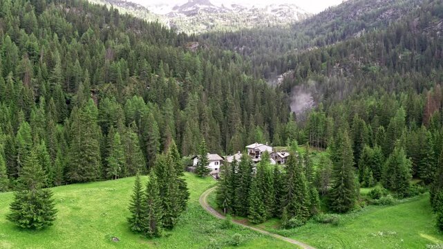 Cascate del rutor's lush green forest and a winding path leading to a secluded house, aerial view