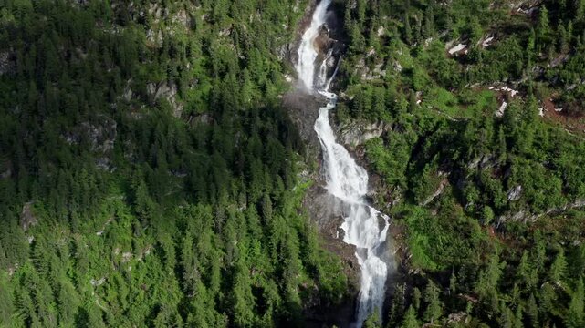 Cascading waterfall flowing through lush green forest in Cascate del Rutor, aerial view