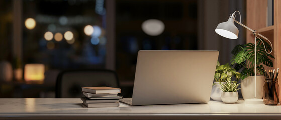 A laptop computer on a table in a dark room at night, illuminated by a table lamp.