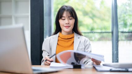 A beautiful Asian businesswoman is reading and reviewing business financial reports at her desk.