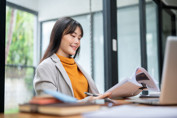 A beautiful Asian businesswoman is reading and reviewing business financial reports at her desk.
