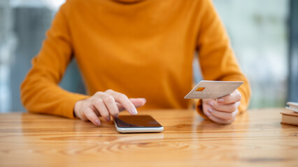 A close-up image of a woman holding a credit card and using her smartphone, paying bills online.