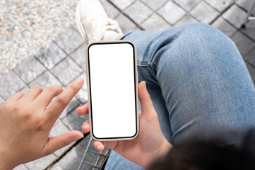 Top view image of a woman in jeans sitting outdoors, using her smartphone, touching on the screen.