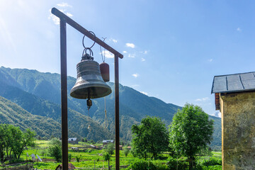 Two bells hang on a frame made of iron pipes in the church yard. Mountain scenery is in the background.