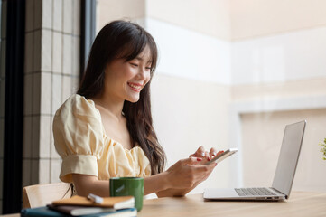 A beautiful Asian woman using her smartphone at her desk, using her smartphone while working.